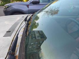 A car with a dirty windshield and a reflection of a building in the window. The car is parked next to a grey suv photo