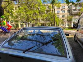 A car with a windshield wiper is parked in front of a building. The car is parked in a parking lot next to a playground photo