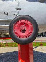 A red wheel on a plane is shown. The wheel is black and red, and it is on a red post. The image has a vintage feel to it, and it seems to be a close-up of the wheel photo