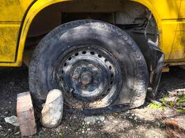 A yellow school bus tire is missing a piece. The tire is black and has a hole in it. The tire is on the ground and is surrounded by rocks photo