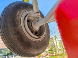 A tire is hanging from a pole. The tire is black and the pole is red. The tire is upside down and the pole is leaning against a wall photo