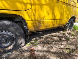 A yellow van with a flat tire is parked on the side of the road. The tire is missing and the van is covered in dirt photo