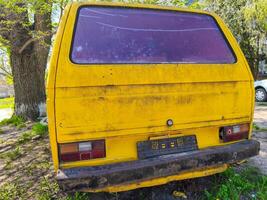 Yellow van with red window and license plate. The van is parked in a grassy area. photo