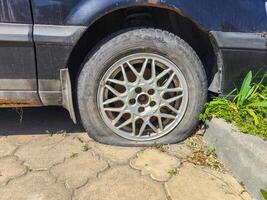 A car tire is flat and has a hole in it. The tire is on a cement surface photo