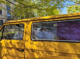 A yellow van with a purple tinted window. The van is parked in front of a building photo