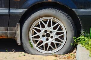 A black car with a flat tire. The tire is missing a piece and is sitting on the ground photo
