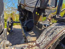 A rusted old tractor with a black engine. The engine is missing a few bolts and the front of the tractor is missing a wheel photo