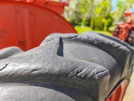 The tire of a tractor is old and has a noticeable black spot on it. The tire is made of rubber and has a worn appearance, with grooves and ridges visible on its surface photo