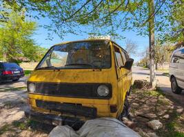 A yellow van is parked in a grassy area. The van is dirty and has a broken window. The scene is quiet and peaceful, with no other vehicles in the area photo