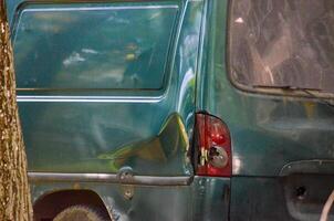 A green van with a smashed rear end. The van is parked next to a tree. The front of the van is damaged, and the back end is missing photo
