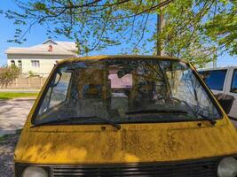 A yellow car with a broken window sits in a parking lot. The car is dirty and has a heart drawn on it photo