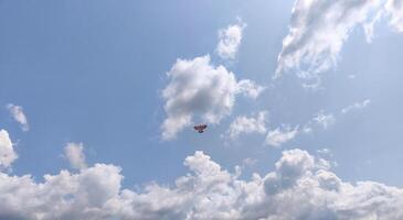 A red plane is flying through a cloudy sky. The sky is mostly blue with some clouds scattered throughout. Scene is peaceful and serene, as the plane soars through the sky above the clouds photo