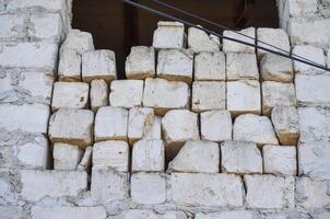 A wall made of white bricks with a hole in it. The bricks are stacked in a way that they are not in a straight line photo