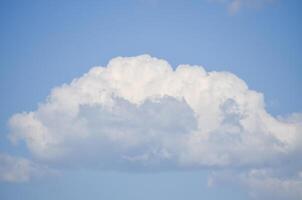 A large cloud in the sky with a blue sky background. The cloud is white and fluffy. The sky is clear and bright, with no signs of rain or storm. Concept of calm and tranquility photo