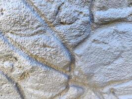 The image is of a wall with a grey and white texture. The wall appears to be made of stone or concrete, and it has a rough, uneven surface. The wall is not painted, and it has a natural photo