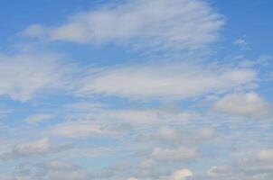 The sky is blue with many clouds. The clouds are scattered throughout the sky, and some are larger than others. Scene is calm and peaceful, as the clouds are not too dense and the sky is mostly clear photo