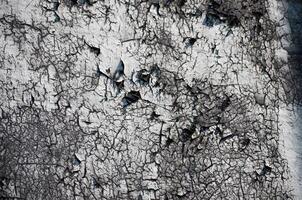 A wall with a lot of holes and cracks. The wall is gray and white. The cracks are deep and the holes are large photo