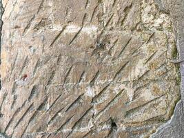 A stone wall with a lot of cracks and holes. The wall is covered in moss and has a rough texture photo