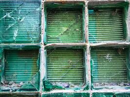 A broken window with a green frame. The window is shattered and the frame is cracked. Scene is one of destruction and decay photo