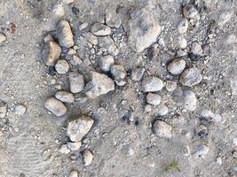 A pile of rocks on a sandy surface. The rocks are scattered and uneven, creating a rough and uneven texture. Concept of ruggedness and naturalness, as if the rocks have been left there by the elements photo