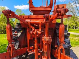 A red tractor with a black frame. The tractor is old and rusty. The tractor is parked in a field photo