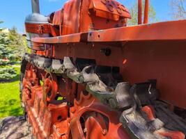 The red tractor has black tracks and is parked in a grassy area. The tracks are worn and dirty, indicating that the tractor has been used for a long time. The tractor is a vintage model photo