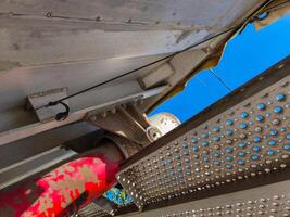 A red pipe is attached to a metal beam. The beam is covered with a mesh of holes photo