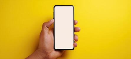 Hand holding a smartphone with blank screen on yellow background photo