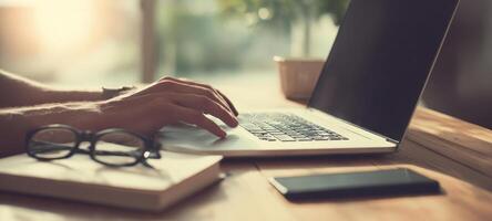 The laptop resting on a wooden desk with hands typing and smartphone nearby. photo