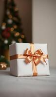 white gift box with a gold ribbon and a christmas tree in the background photo