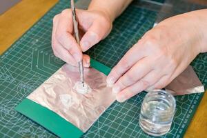 Hard work of jeweler on intricate silver pendants. Hands guide the tool, creating intricate design. photo
