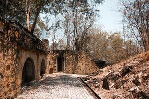 Stone pathway leads toward stone structure surrounded by trees. Rustic design with arched entrance. photo