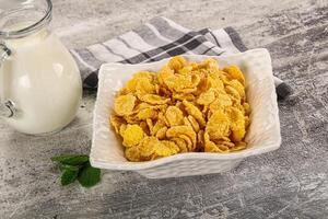 Corn flakes and milk in a bowl and a glass of milk on a wooden table photo