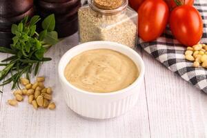 A bowl of peanut butter next to tomatoes, nuts and other ingredients photo