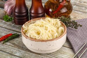 Noodles in a bowl with chopsticks and bottles on a wooden table photo