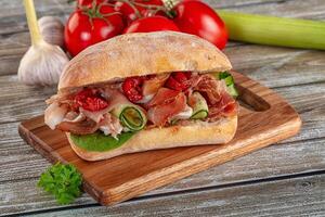 A sandwich on a wooden cutting board with tomatoes and cucumbers photo