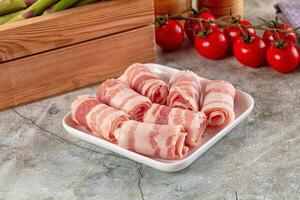 A plate of bacon rolls on a counter next to a basket of tomatoes photo