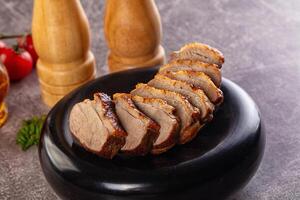 Sliced pork on a black plate with a wooden cutting board photo