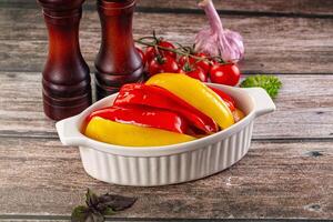 A white dish with peppers and garlic on a wooden table photo