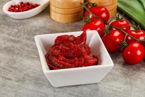 A bowl of red sauce next to a bowl of tomatoes photo