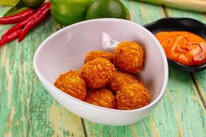 A bowl of fried chicken balls with a spoon and some peppers photo