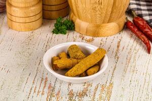 A bowl of pickles on a table next to a wooden chopping board photo