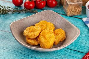 A bowl of fried chicken on a table next to a bowl of tomatoes photo