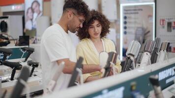 Smiling couple browsing hair dryer selection in modern electronics store, comparing product features while making purchasing decision together video