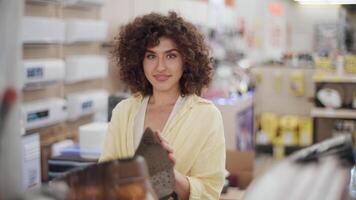 Young woman carefully selecting premium iron in electronics store, meticulously examining device features and design while contemplating household appliance purchase video