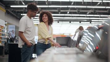 Young couple browsing laptop selection in modern electronics store, sharing excitement while comparing devices and making joint purchase decision video
