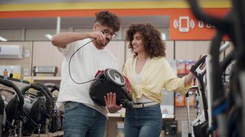 Young couple examines vacuum cleaner features in an electronics store, engaging with product details. Slow-motion focus on modern consumer behavior video