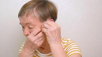 An elderly woman puts a hearing aid on her ear. Problems of aging and deafness. The use of medical technologies to support the hearing of elderly people with disabilities video