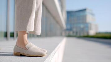A stylish individual showcases a summer outfit with raffia mules and neutral trousers on a clean sidewalk photo