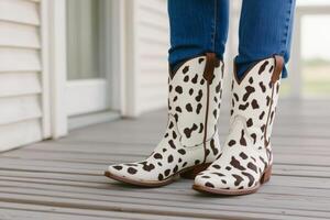 Unique fabric boots with cow pattern rest on wooden porch next to country style house under bright sunlight photo